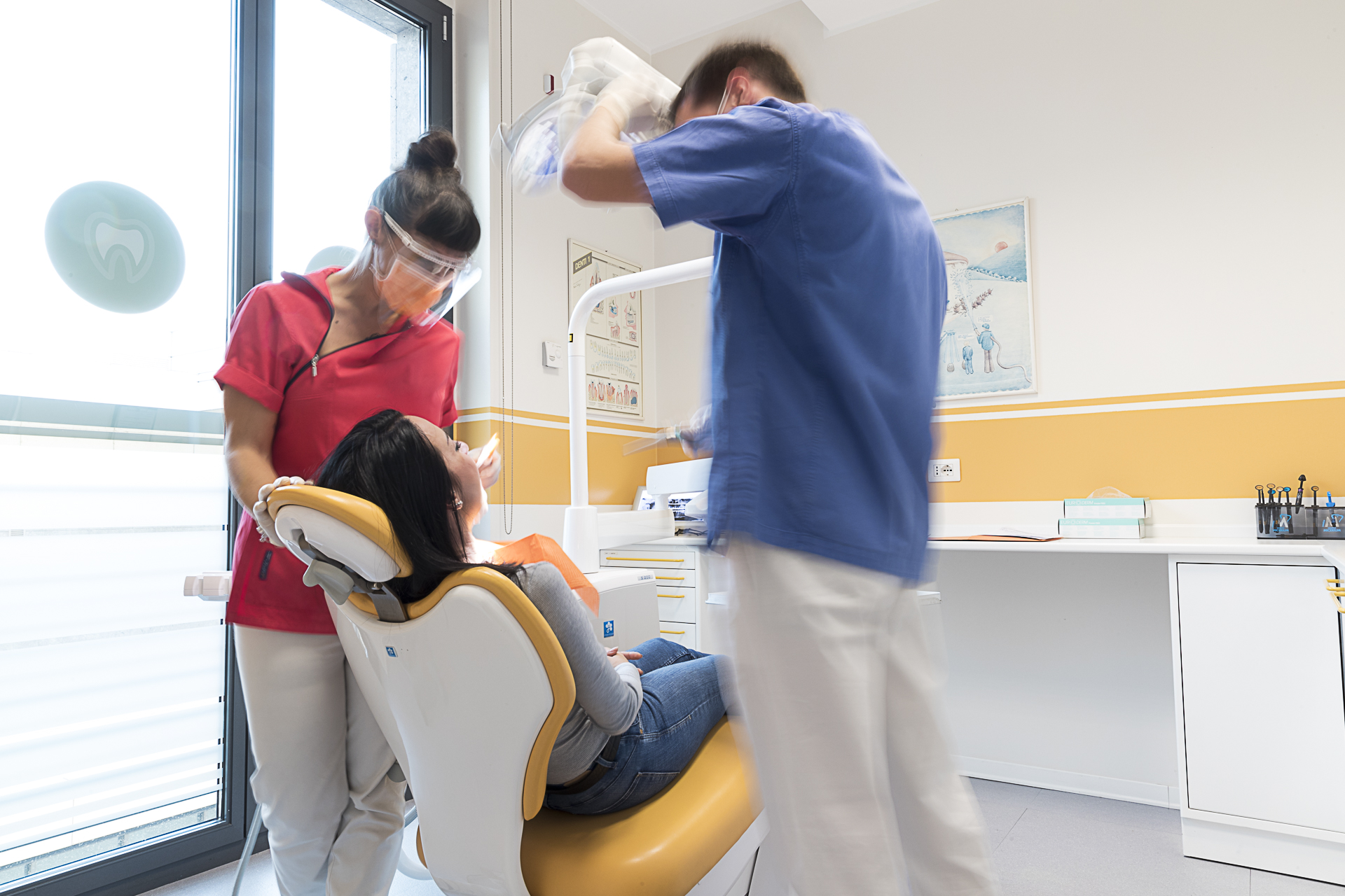 Un odontoiatra e un'assistente durante una visita, in una sala dello studio con le pareti gialle
